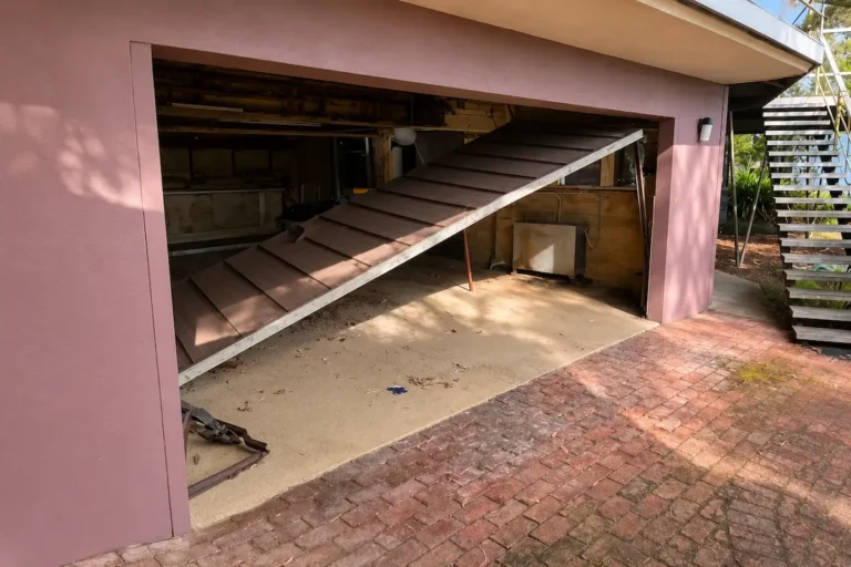 Damaged sectional garage door after a vehicle impact, showing severe panel damage requiring assessment to determine whether repair or replacement is the safest option.