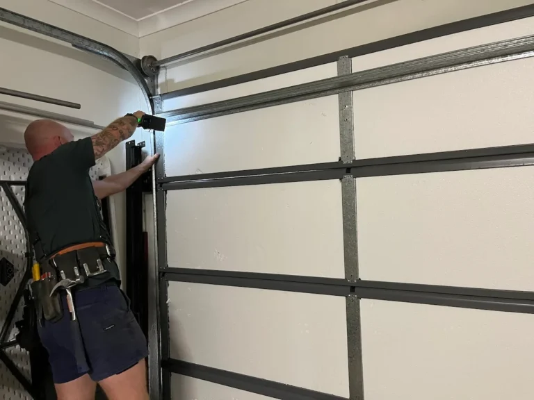 Garage door technician servicing a sectional garage door by tightening hardware to help prevent rattles, vibration and excessive noise.