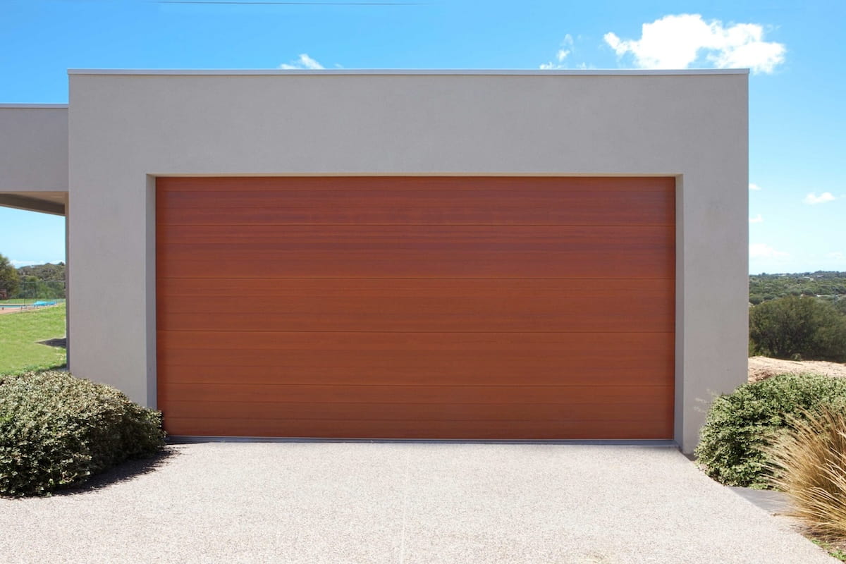 Gliderol sectional garage door featuring a Tuscan profile in a Native Maple woodgrain finish, showcasing a clean, modern flush panel design on a contemporary home exterior.