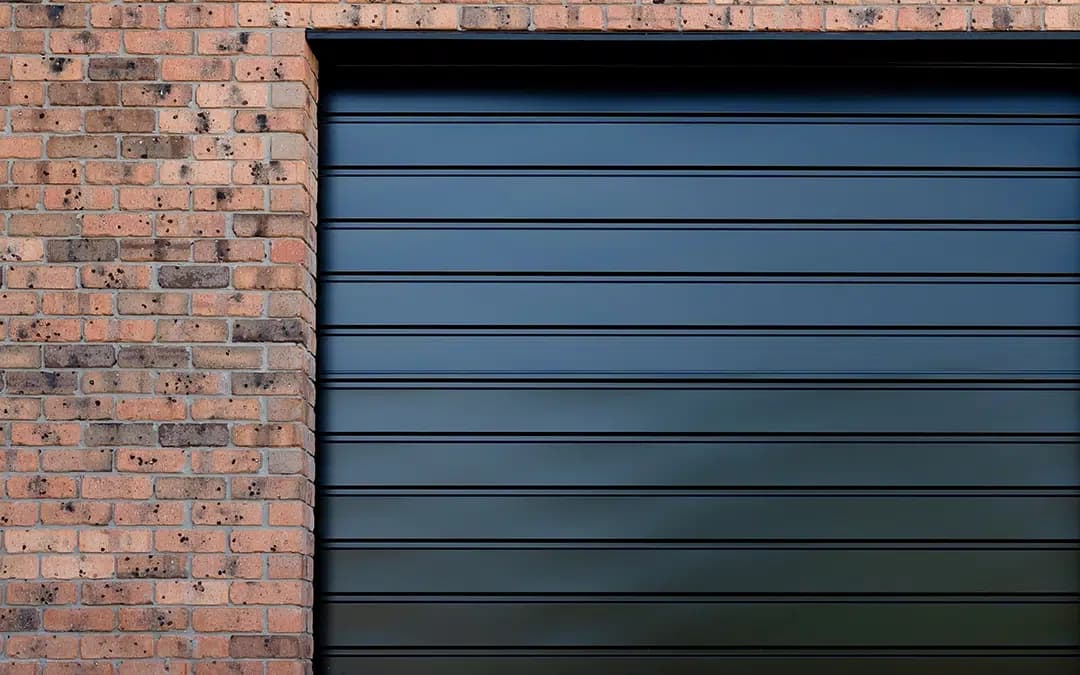 Close-up detail of a dark charcoal roller garage door installed against a brick wall, highlighting its compact profile and durable construction.